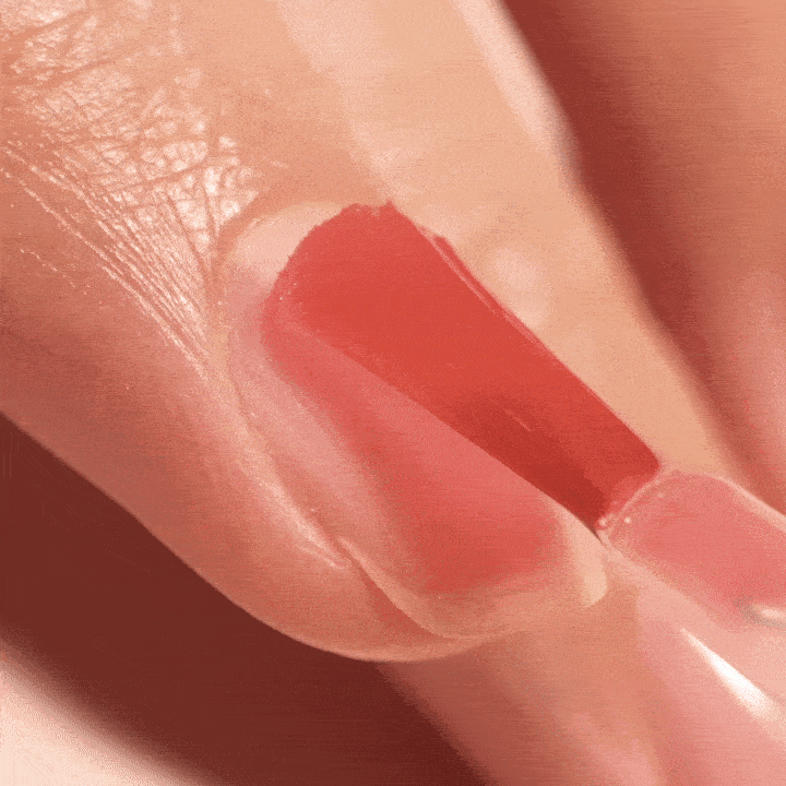A close-up of a hand as red nail polish is being smoothly applied to a fingernail with a brush.