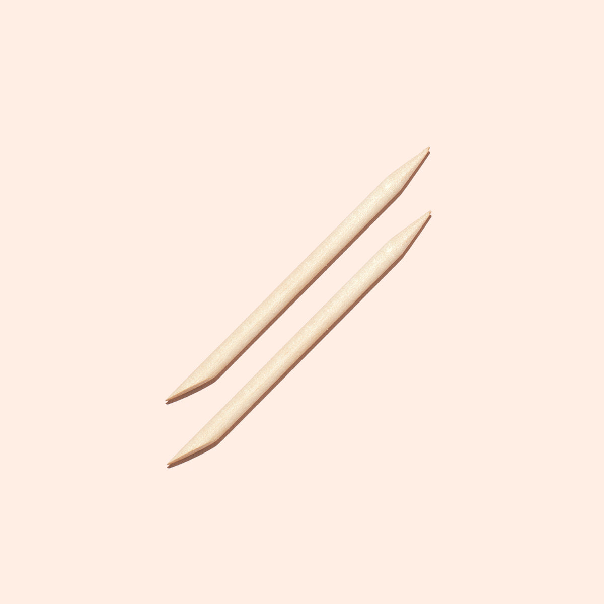 Deux bâtonnets à cuticules en bois Manucurist US (x2), chacun doté d’une extrémité pointue et d’une extrémité biseautée, sont placés parallèlement l’un à l’autre sur un fond beige pâle.