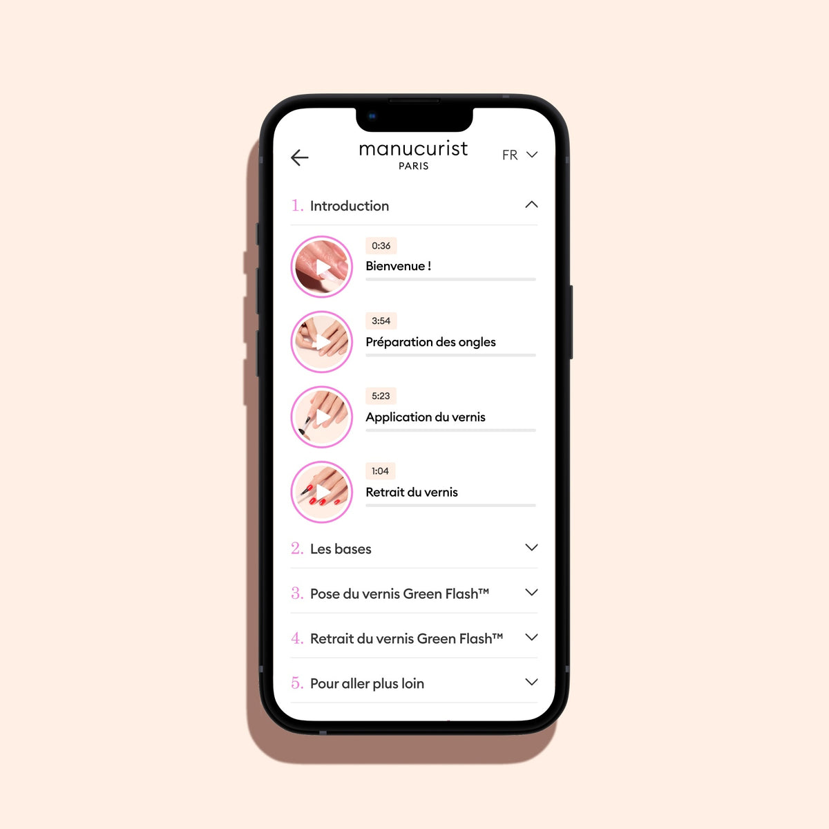 Un smartphone avec un cadre noir sur fond beige affiche l’application de vidéos de formation de Manucurist-test, avec des icônes et des étapes chronométrées — introduction, préparation des ongles, application du vernis et retrait — dans un tutoriel vidéo de manucure française étape par étape.