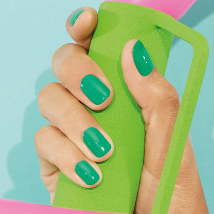 A hand with neatly manicured nails painted in Manucurist’s Brazil, an electric green shade, and finished with Top Coat holds a green foam handle against a light blue background.