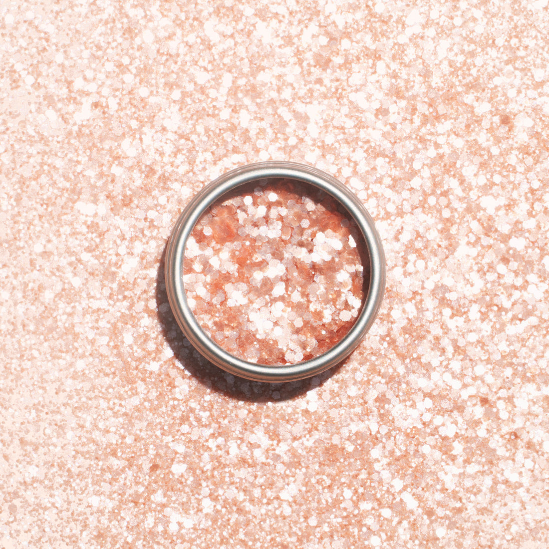 A silver ring rests on a pale pink surface dusted with Manucurist’s Blush Biodegradable Glitter, shimmering through the ring and all around it.