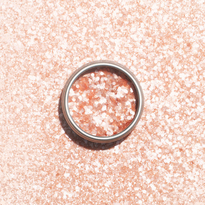 A silver ring rests on a pale pink surface dusted with Manucurist’s Blush Biodegradable Glitter, shimmering through the ring and all around it.