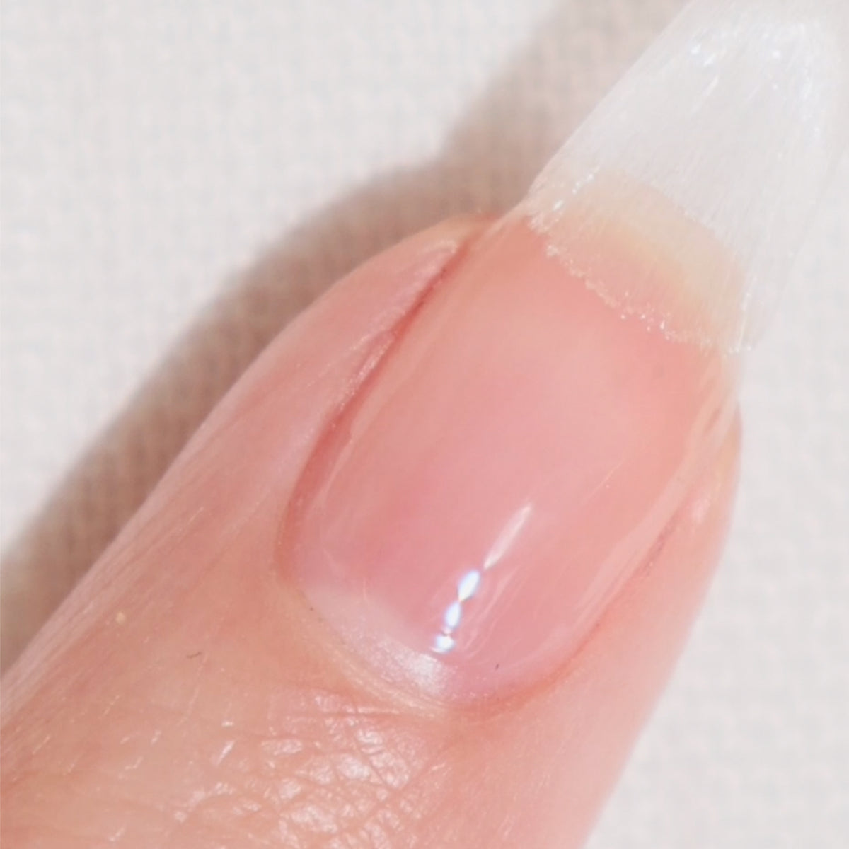A close-up of a fingernail being painted with clear nail polish; the brush is visible at the top edge of the nail.