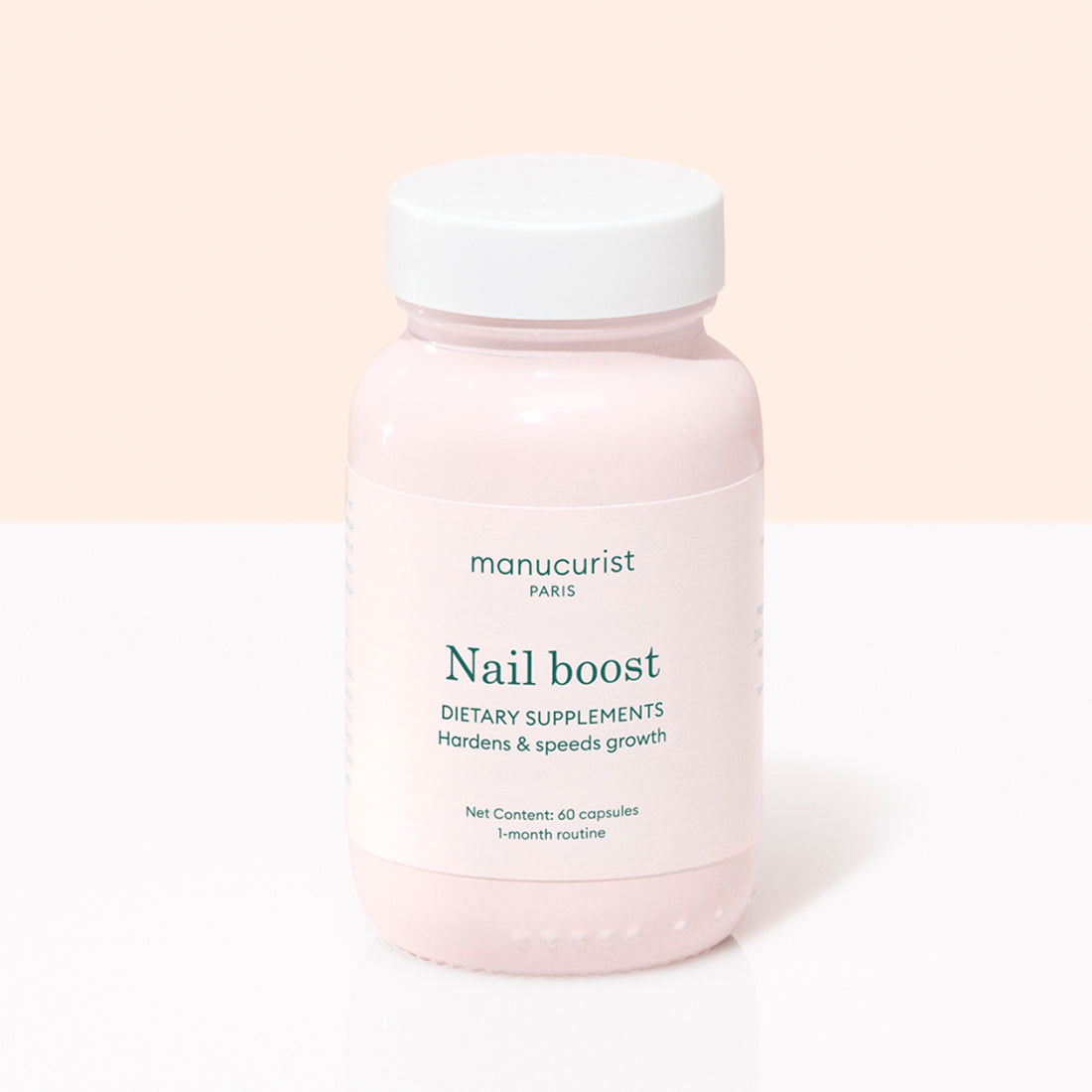 A pink bottle labeled Manucurist Nail Boost contains 60 nail supplement capsules for a 1-month routine, designed to strengthen and speed nail growth. Features a white cap and is set against a light pink and white background.