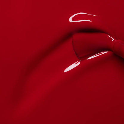 A close-up of the glossy, deep red "Dark Dahlia" gel polish by Manucurist, highlighting its smooth curves and subtle reflections, reminiscent of latex stretched over a form.