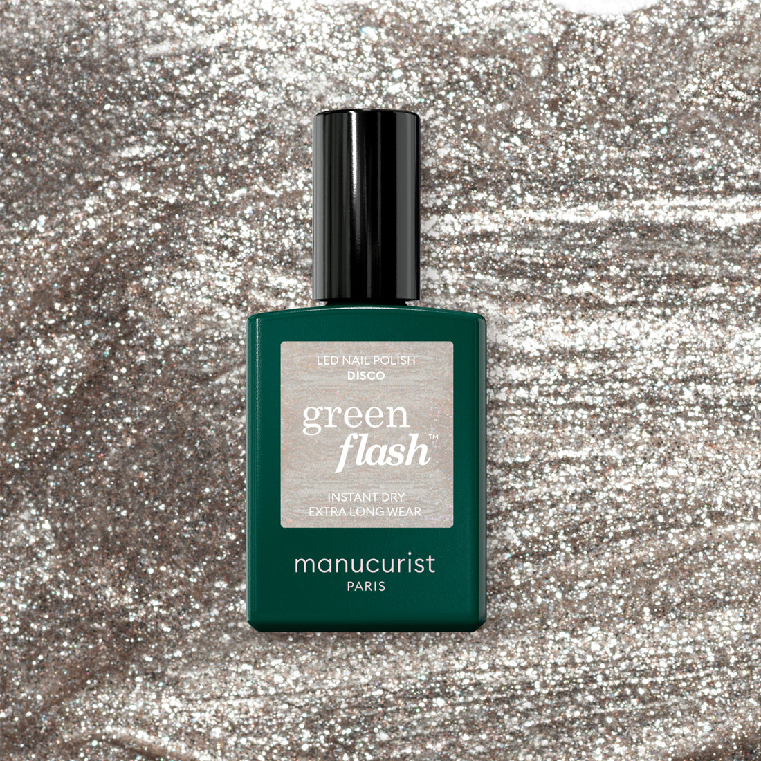 A Manucurist Disco gel polish bottle sits on a shimmering silver background. The bottle is dark green with a black cap and features a sparkly silver label.