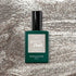 A Manucurist Disco gel polish bottle sits on a shimmering silver background. The bottle is dark green with a black cap and features a sparkly silver label.
