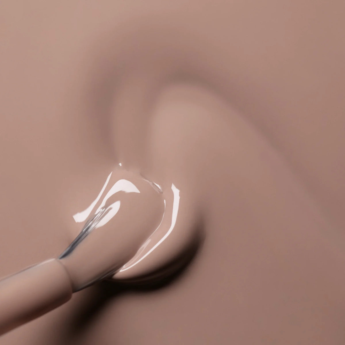 A close-up of a nail polish brush spreading light beige nail polish onto a smooth surface, creating a glossy and creamy texture.