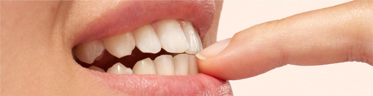 Close-up of a person biting their index finger gently between their front teeth, showing clean, natural teeth and part of their lips and finger.