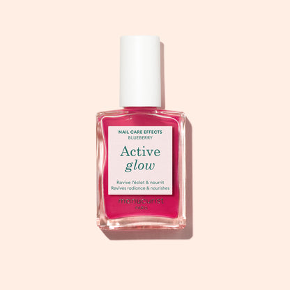 A pink bottle of Manucurist Active™ Glow Blueberry plant-based nail care polish with a white cap, shown against a light beige background.
