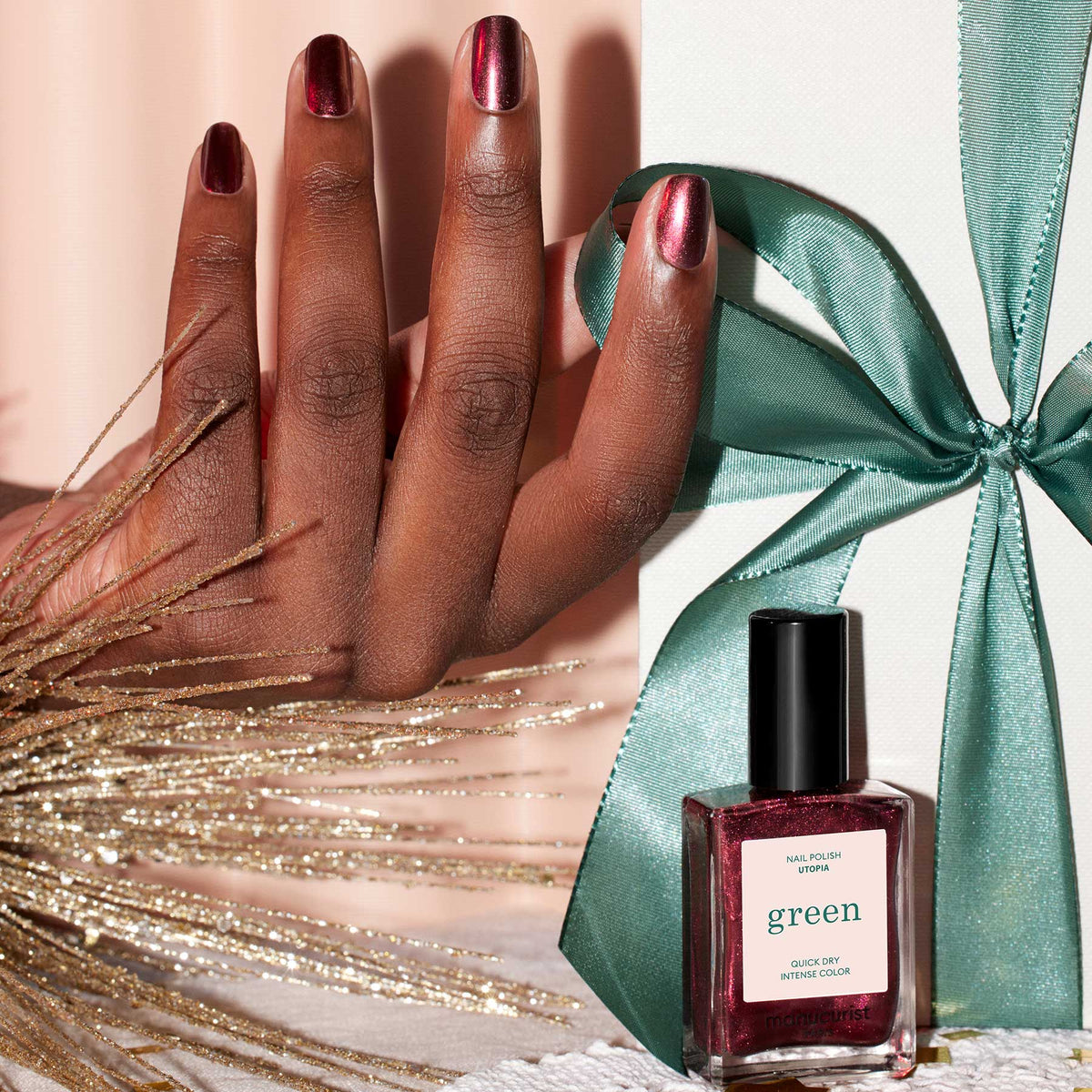 A hand with glossy, metallic crimson nails painted with Manucurist&