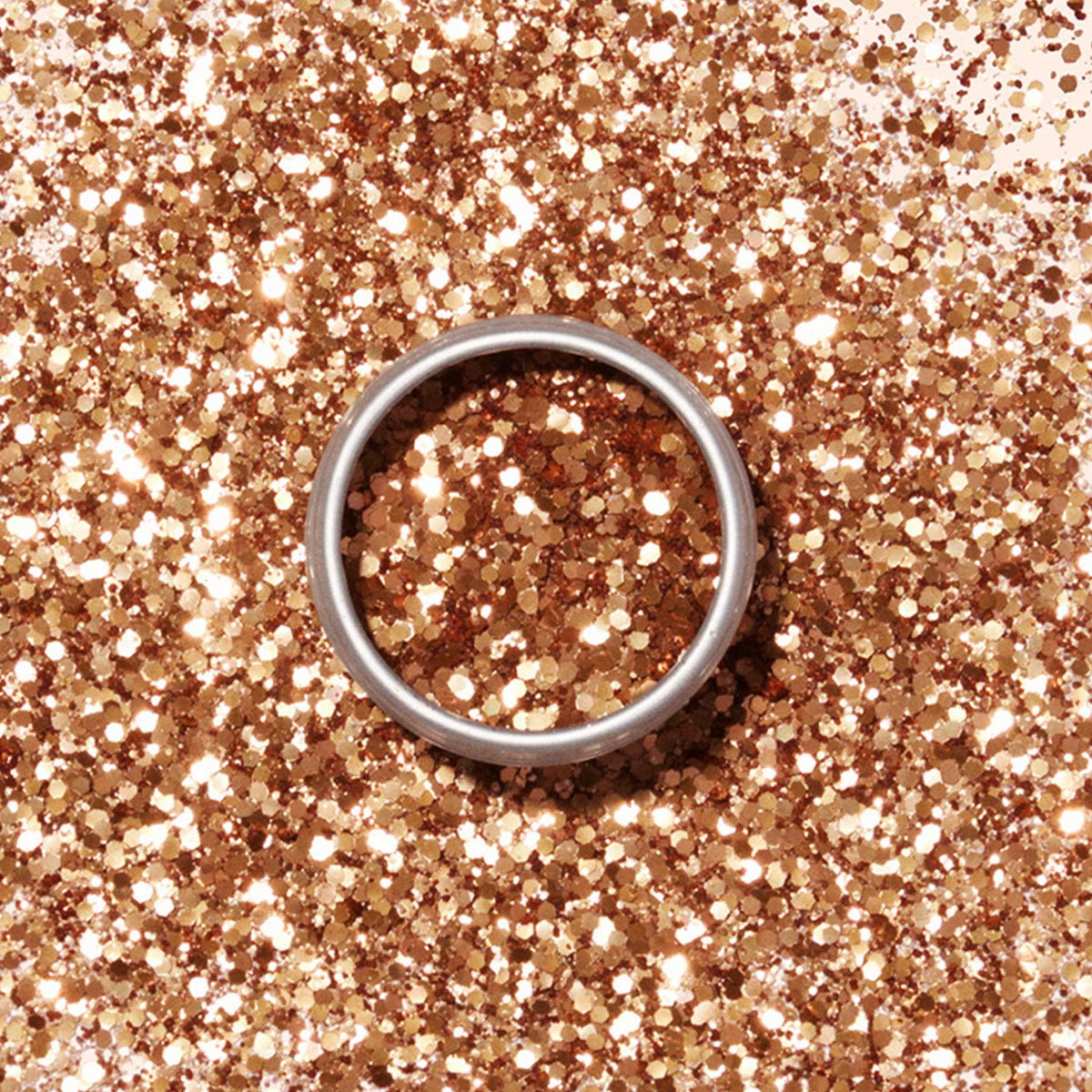 Une bague en argent repose sur une surface saupoudrée de Paillettes Biodégradables Cuivre Manucurist, dont l&
