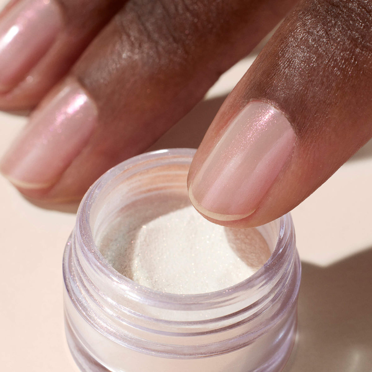 Gros plan sur une main aux ongles roses scintillants qui plonge un doigt dans un petit pot de Glitter Trio - Rose Gold de Manucurist, une fine poudre de paillettes blanches parfaite pour le Nail Art ou le maquillage.