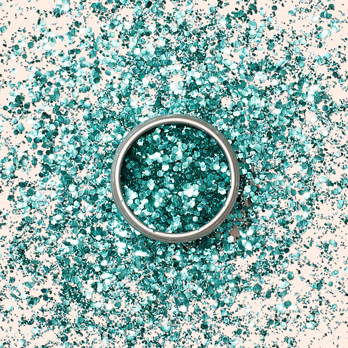 Une bague en argent repose sur un tas de Paillettes Biodégradables Manucurist bleu canard, dispersées sur une surface claire.
