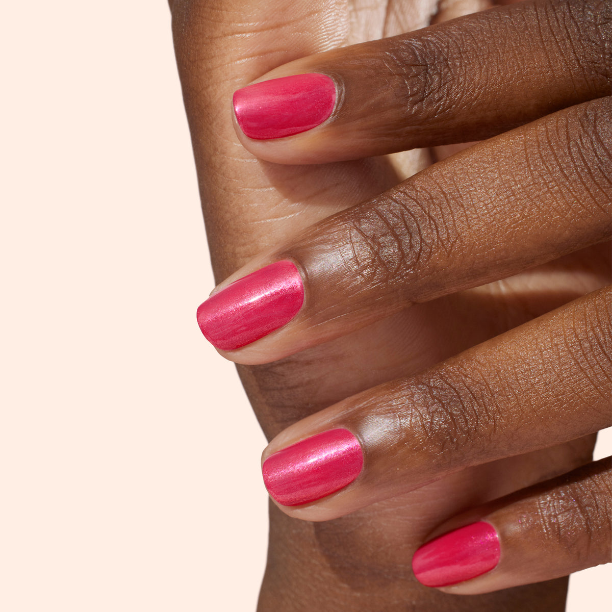 A close-up of a hand with medium-dark skin tone, showing neatly manicured nails painted with glossy pink nail polish against a light background.