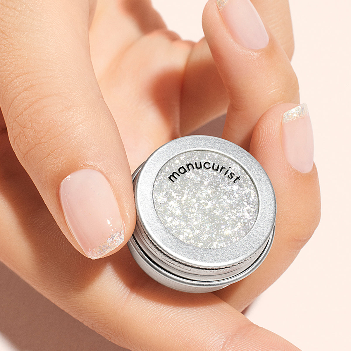 Une main aux ongles rose pâle délicatement pailletés d&