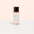 A small bottle of Manucurist Degreaser, a plant-based nail prep with clear pink liquid and black cap, sits on a reflective white surface. Its white label with green and pink text stands out against a pale peach background.