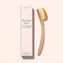 A Dust Brush by Manucurist with vegan bristles and a curved wooden handle sits beside its tall box labeled “Bye bye dust – Dust Brush” on a light beige background.