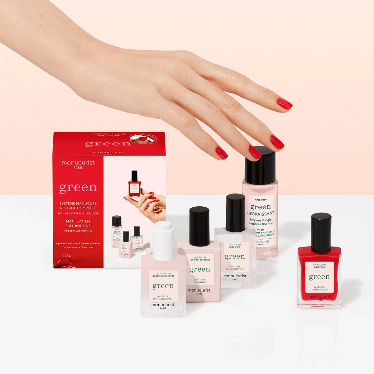 A hand with red-painted nails hovers above Manucurist manicure products, including three plant-based nail polishes, a red gel effect polish, and the pink-and-red Discovery Kit box, set on a white surface against a soft pink background.