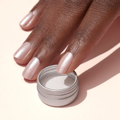Une main aux ongles rose pâle et irisés arborant un subtil effet glazed blanc créé avec la Poudre Effet Glazed Blanc de Manucurist repose à côté d&
