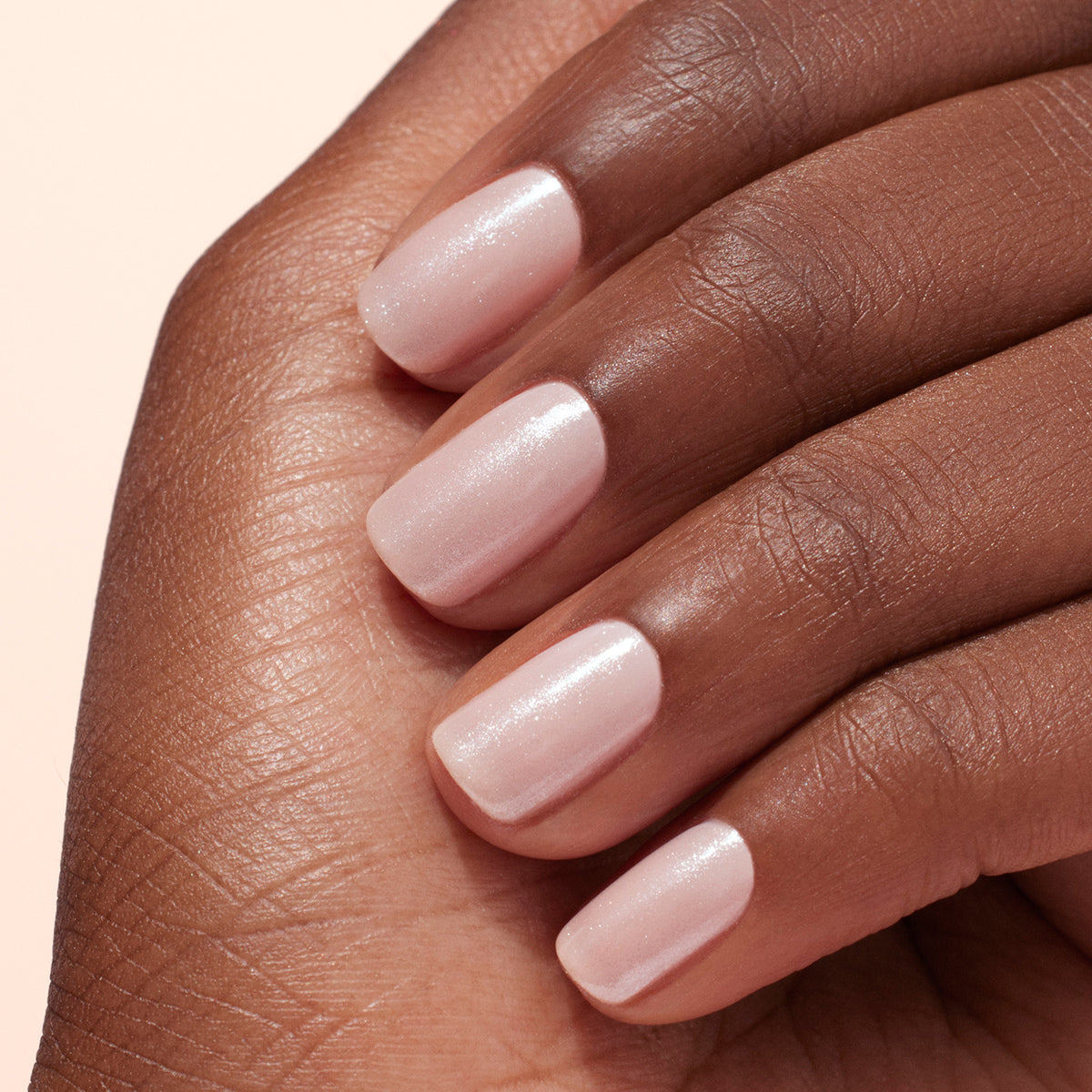 Gros plan sur une main à la peau mate, arborant des ongles courts et soignés vernis de rose pâle et sublimés par la Poudre Effet Glacé Blanc de Manucurist pour un éclat subtil et une manucure élégante.