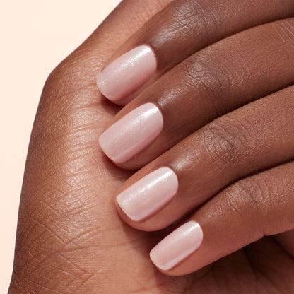Gros plan sur une main à la peau mate, arborant des ongles courts et soignés vernis de rose pâle et sublimés par la Poudre Effet Glacé Blanc de Manucurist pour un éclat subtil et une manucure élégante.