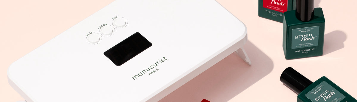 A white Manucurist Paris nail lamp is shown on a light pink surface, surrounded by several green and red bottles of Green Flash nail polish.