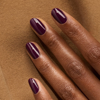A close-up of a dark-skinned hand resting on brown fabric, featuring neatly manicured nails painted with Manucurist&