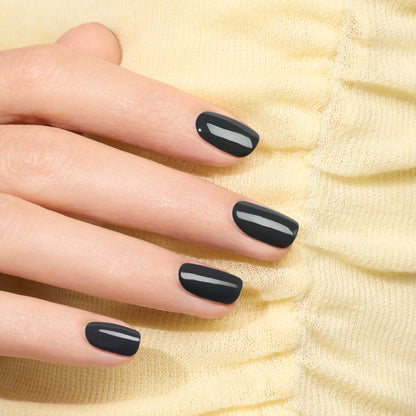 A hand with neatly manicured nails painted in glossy Anthracite by Manucurist rests on soft, light yellow textured fabric.