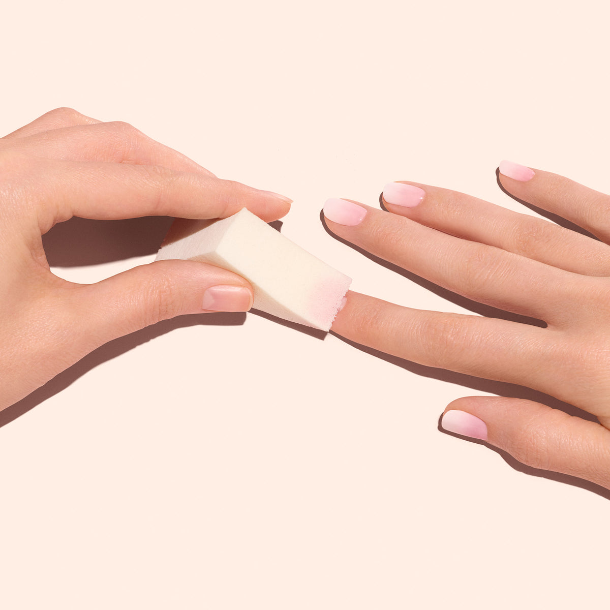 Une main utilise les Éponges Nail Art Manucurist (x4) pour estomper un vernis rose clair, créant un effet Baby Boomer délicat sur les ongles de l&