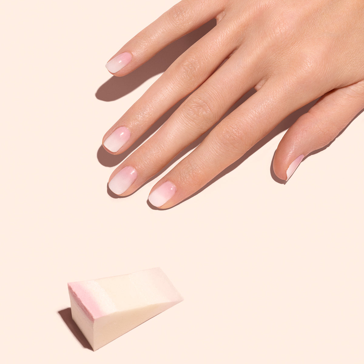 Une main aux ongles naturels soigneusement manucurés repose sur une surface claire. À proximité, les éponges Nail Art Manucurist - x4 suggèrent l’outil parfait pour créer des ongles Baby Boomer doux.
