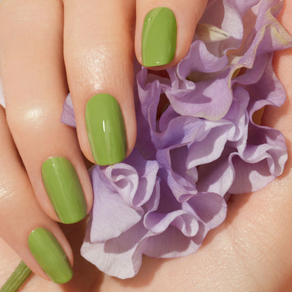 A hand with neatly manicured nails, painted in Manucurist’s Sweet Pea polish, gently holds a soft, pale purple flower.