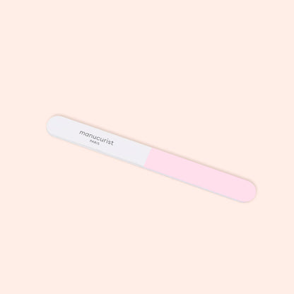 The Manucurist 3-Face Nail Buffer, featuring pink and white sections with "Manucurist" printed on the white side, is shown against a light beige background.