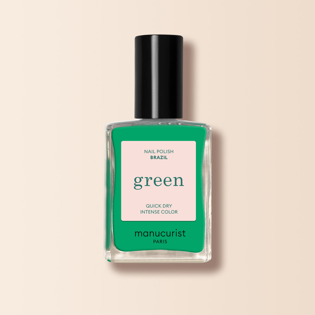 A clear glass bottle of Manucurist Brazil nail polish in electric green with a black cap. The label says Brazil, green, Quick Dry Intense Color, semi-matte finish by Manucurist Paris on a pink and green background. Perfect with your favorite Top Coat.
