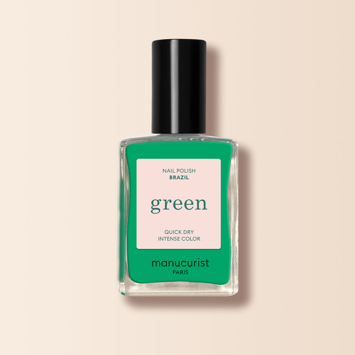 A clear glass bottle of Manucurist Brazil nail polish in electric green with a black cap. The label says Brazil, green, Quick Dry Intense Color, semi-matte finish by Manucurist Paris on a pink and green background. Perfect with your favorite Top Coat.