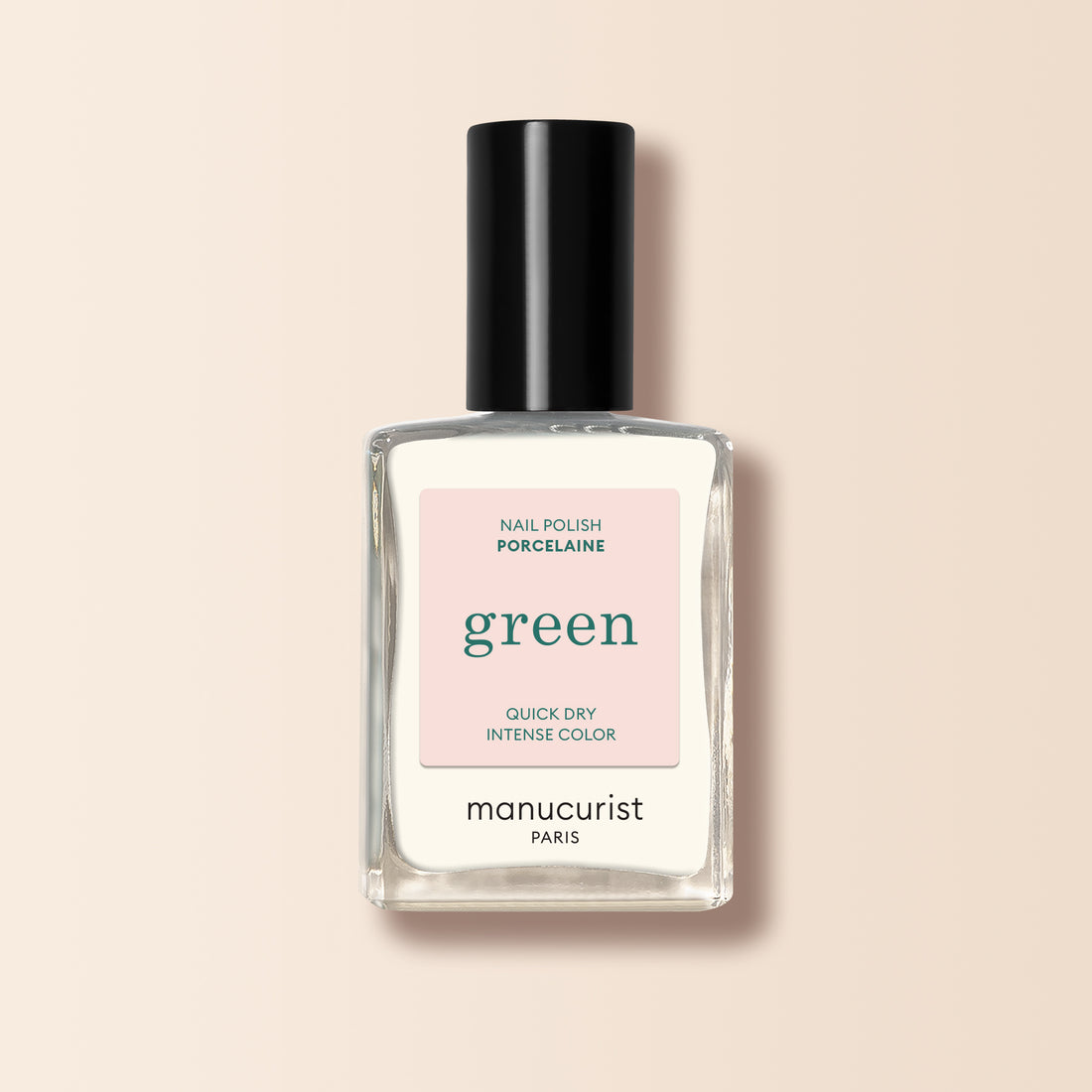Un flacon en verre transparent de vernis à ongles Porcelaine Manucurist au bouchon noir, avec la mention "Quick Dry Intense Color", est présenté sur un fond beige clair.