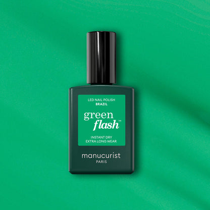Un flacon de vernis LED Manucurist Brazil Green Flash est posé sur un fond vert, avec un séchage instantané et une tenue extra-longue pour des ongles vert électrique éclatants inspirés de la plage de Copacabana.