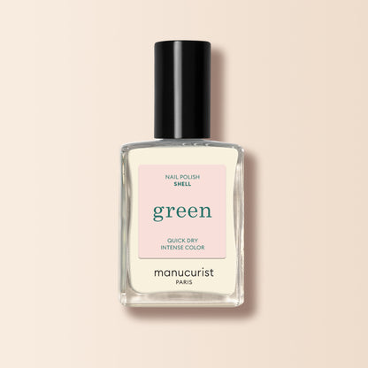 A clear glass bottle of Shell nail polish from Manucurist, with a black cap and light pink label, is displayed against a light beige background.