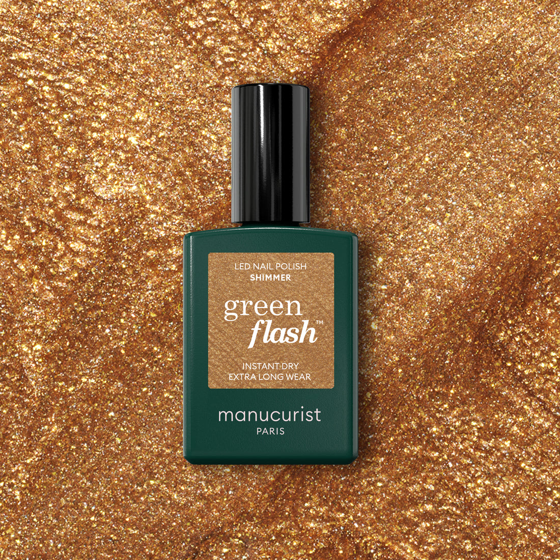 A bottle of Manucurist Shimmer gel polish sits on a sparkling gold surface that matches the cool undertone of the nail polish shade.