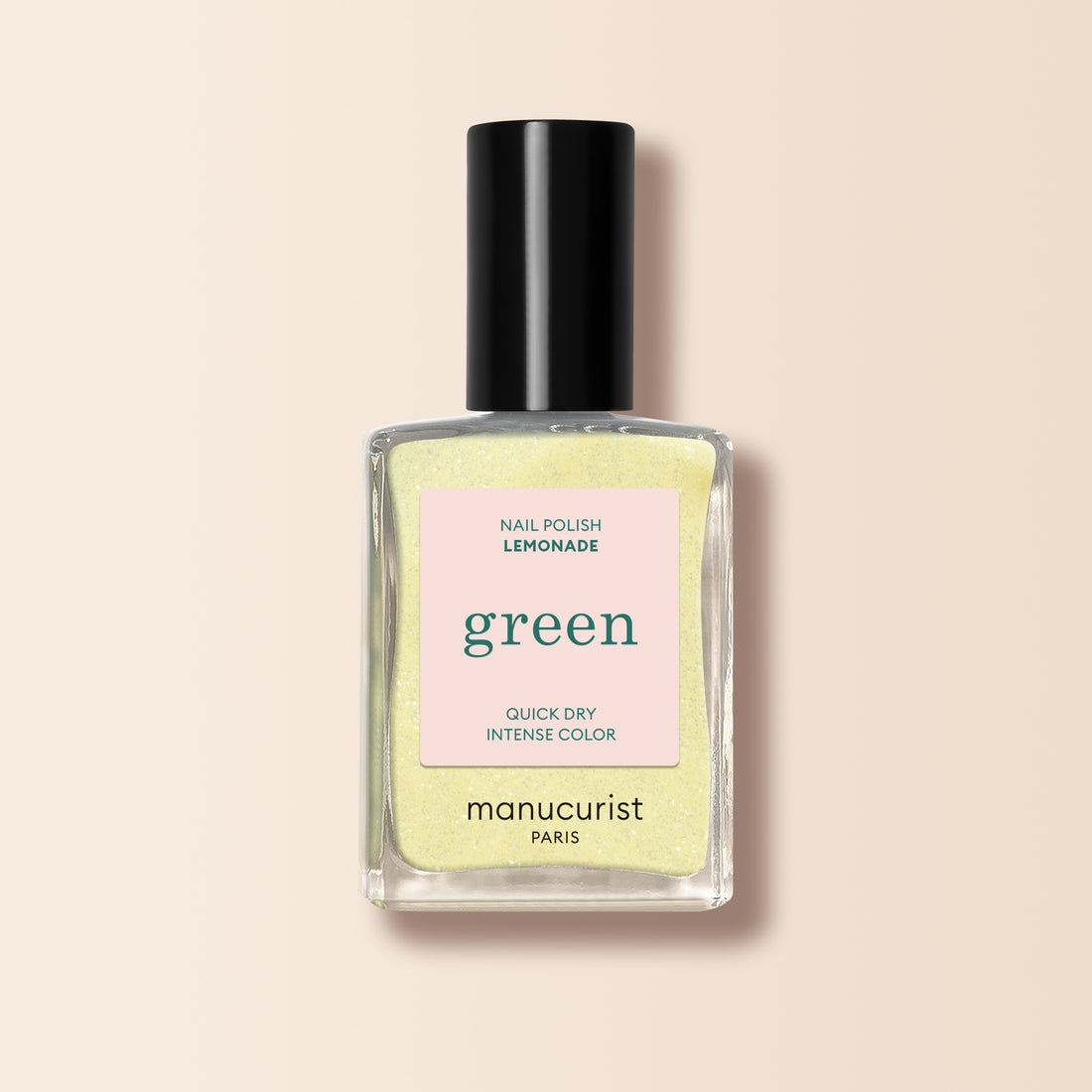 A bottle of Manucurist nail polish in the shade Lemonade, featuring a pale yellow color, black cap, and square label with “green” and “quick dry intense color.”.