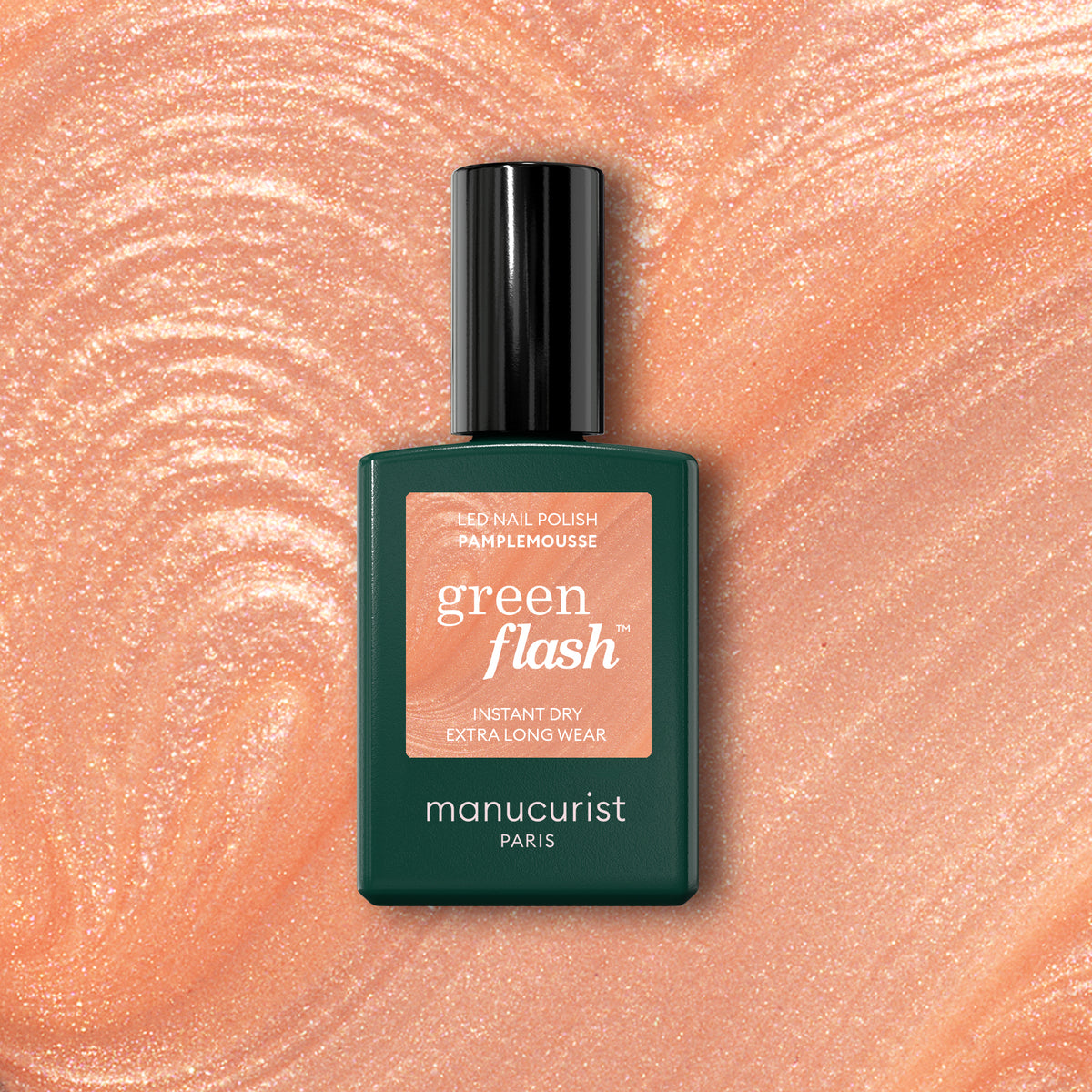 A bottle of Manucurist Pamplemousse nail polish rests on a shimmery, peach-pink background that complements the vibrant shade.