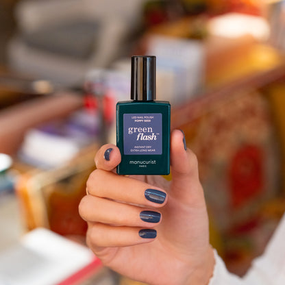 A hand with neatly manicured nails painted in the chic Poppy Seed shade holds a bottle of Manucurist&