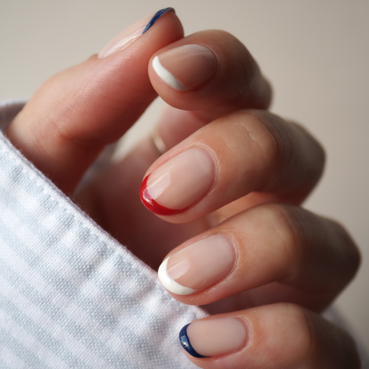 Une main aux ongles courts en amande dévoile le Trio Red, White Blue de Manucurist dans une French manucure minimaliste aux pointes bleues, rouges et blanches. Le look est associé à une manche texturée blanche pour un fini audacieux.