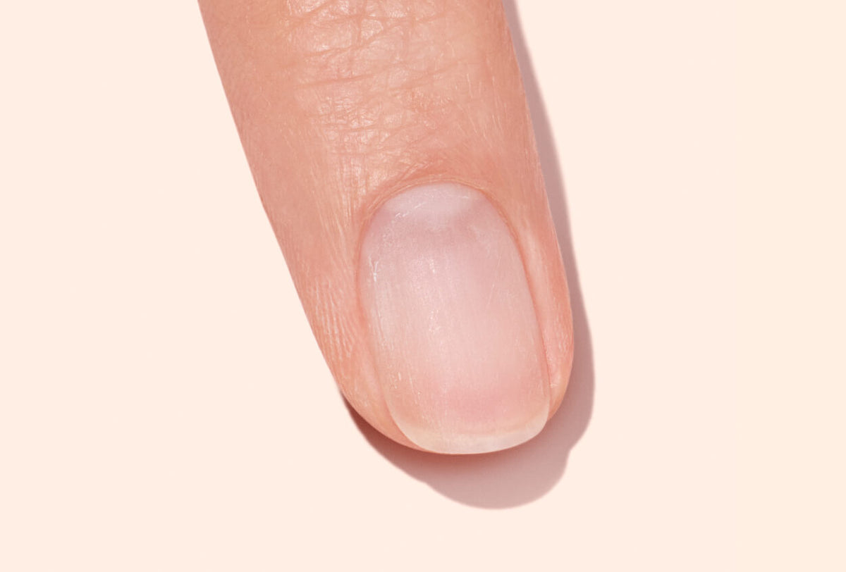 A close-up of a persons fingertip with a neatly trimmed, clean fingernail against a light, neutral background.
