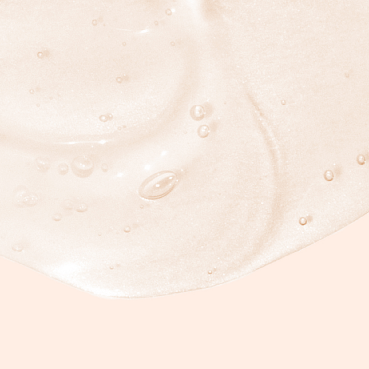 A close-up of a light peach-colored, glossy liquid with small bubbles scattered throughout, spread across a matching peach background.