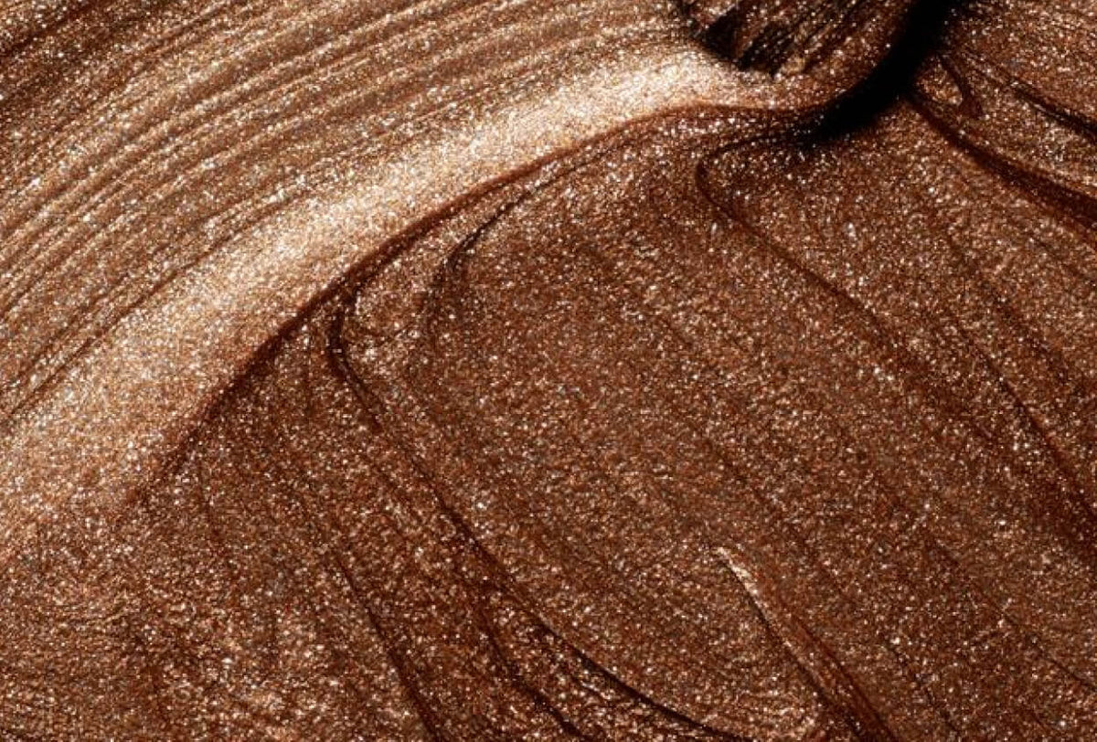 Gros plan sur une crème cosmétique ou un fond de teint bronze ou brun lisse et nacré, avec des traces de pinceau visibles et une texture scintillante.