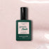 A dark green bottle of Manucurist Gloss gel polish rests on a pale pink, iridescent shimmer background. The label emphasizes instant dry, extra long wear, and high gloss.