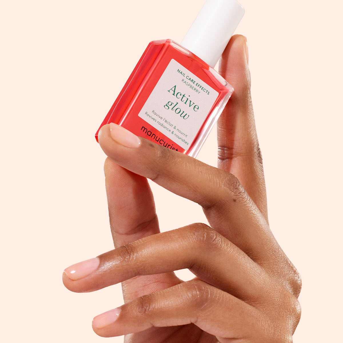 A hand with neatly manicured nails—testament to dedicated nail care—holds a red bottle labeled Manucurist Active™ Glow Raspberry against a pale background.