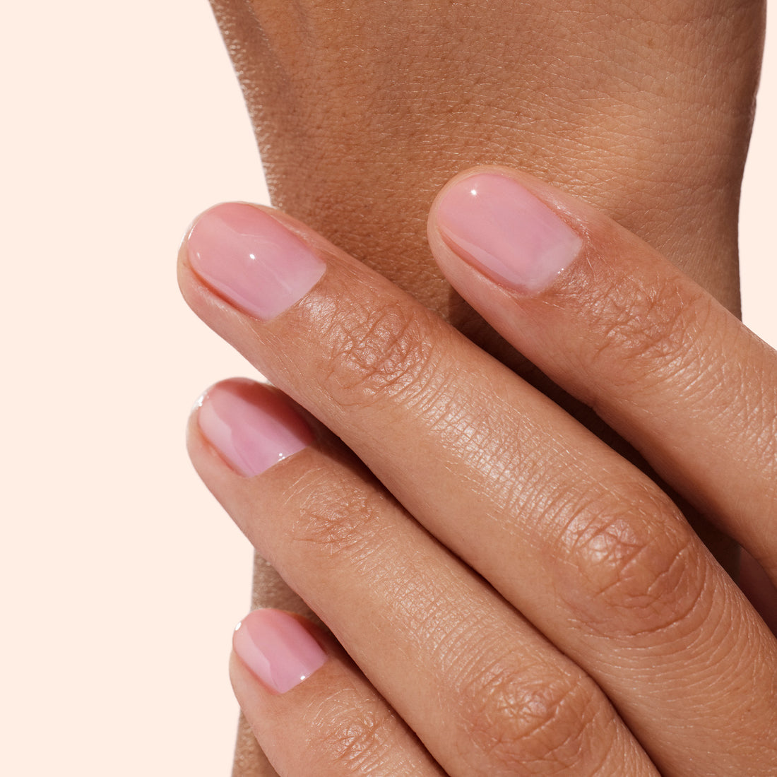A close-up of a hand with neatly manicured nails painted in a light pink, glossy polish—resting gently on another part of the same hand against a neutral background—showcases the naturally healthy, beautiful results achieved with Manucurist Active™ Glow Blueberry nail care.
