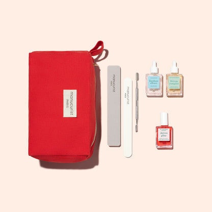 The Manucurist Healthy Glow Duo is shown with a red zippered pouch, gray nail file, white buffer, metal cuticle pusher, and three bottles—including nail polish and cuticle oil—arranged on a beige background.